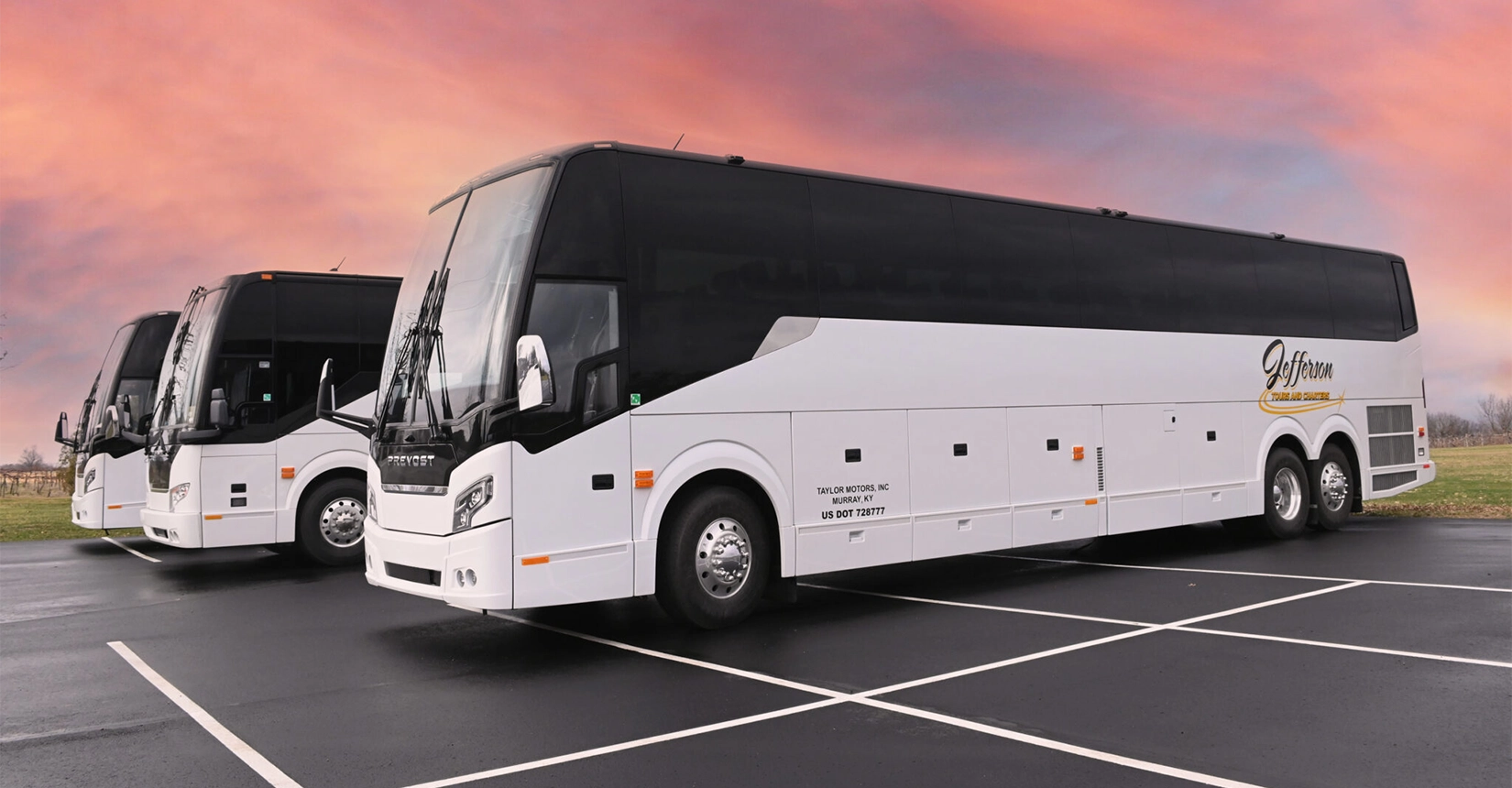 Three white charter buses with Jefferson Tours branding lined up in parking lot against pink and purple sunset sky